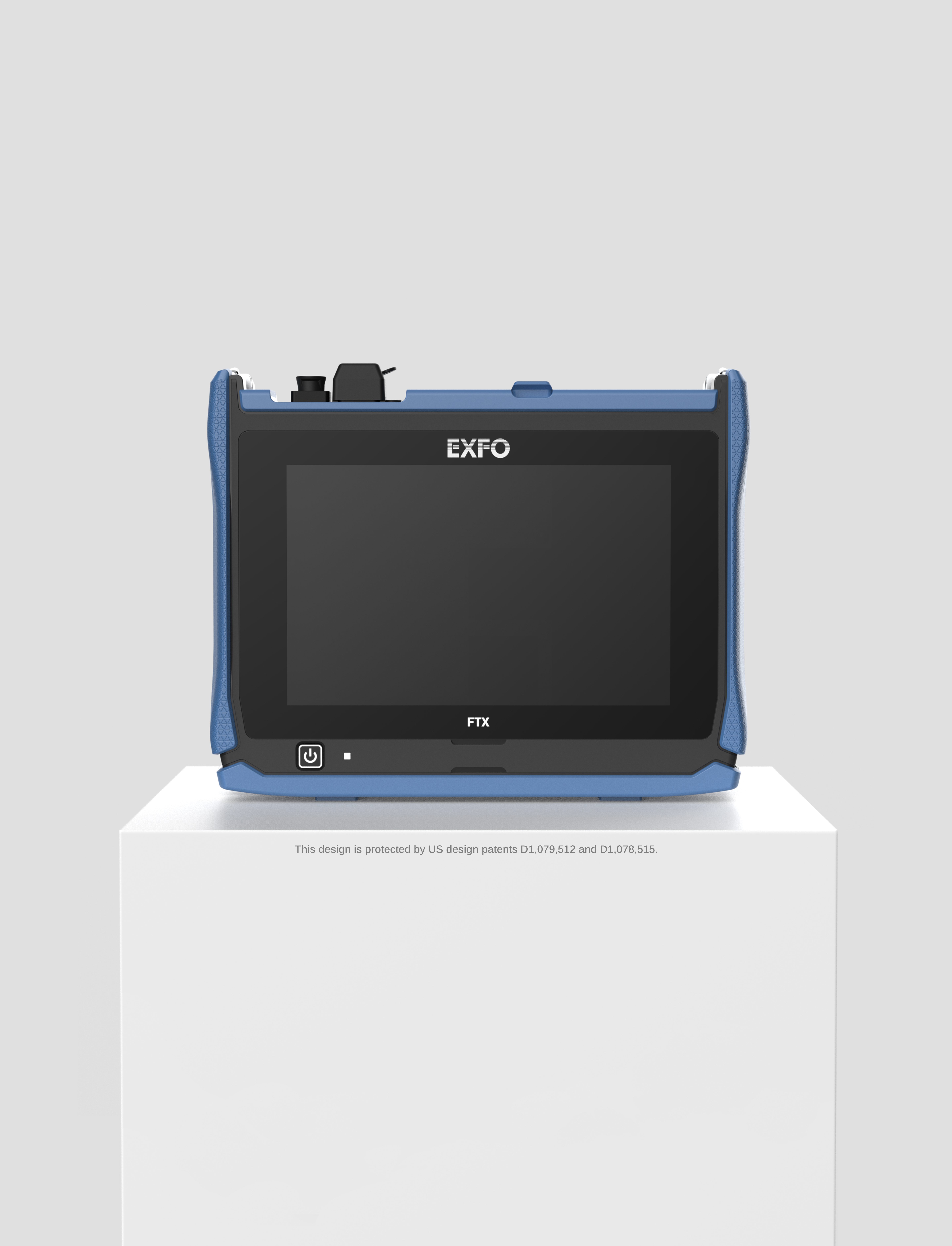 Un appareil électronique EXFO FTX bleu et noir avec un grand écran est posé sur un socle blanc sur fond gris. Le texte situé sous le socle mentionne les brevets d'invention américains.